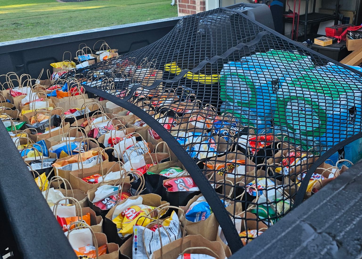 A truck bed packed with rows of sack lunches and cases of bottled water, ready for Saturday