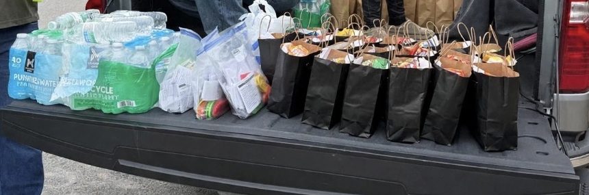 A tailgate lined with sack lunches, hygiene kits and bottled water